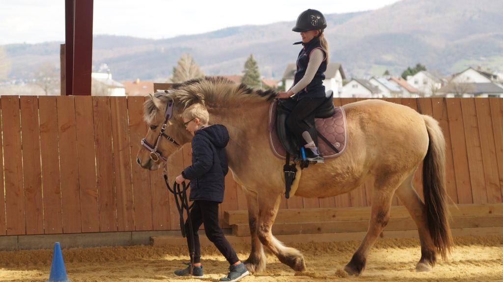 Junge führt Mädchen auf Pferd